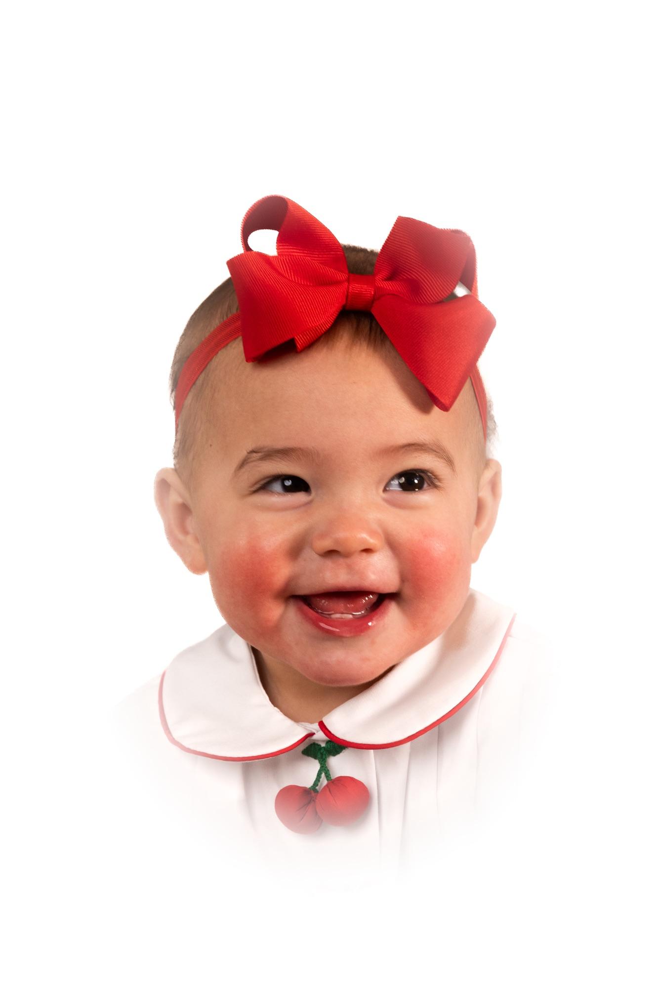 Close studio portrait of a smiling baby in a red bow and cherry-trimmed collar