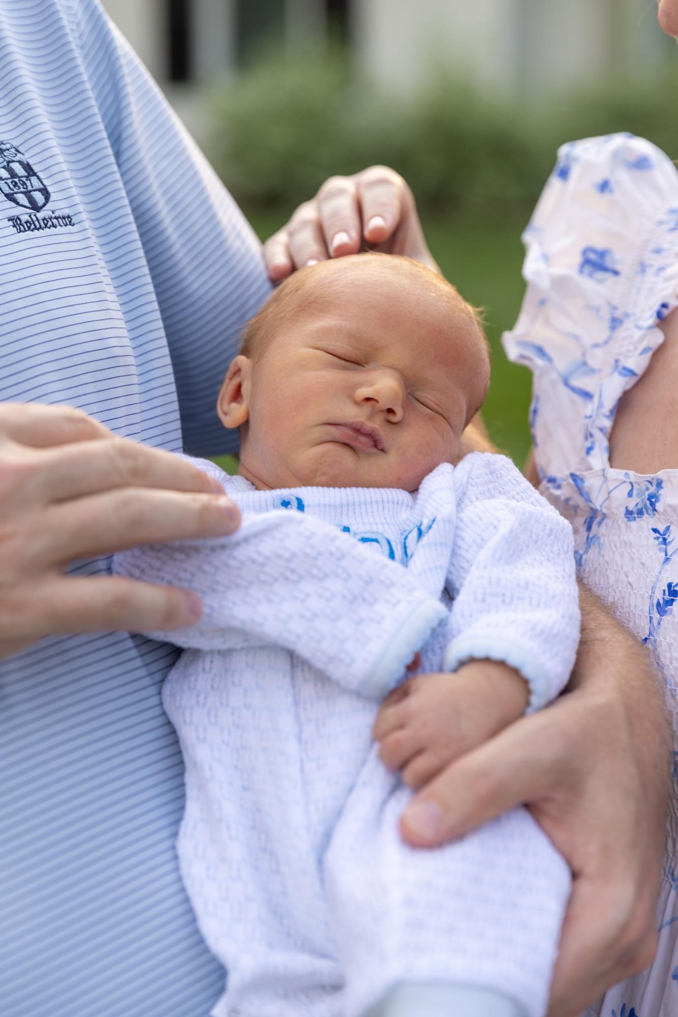 Sleeping newborn cradled between his parents, soft outdoor light