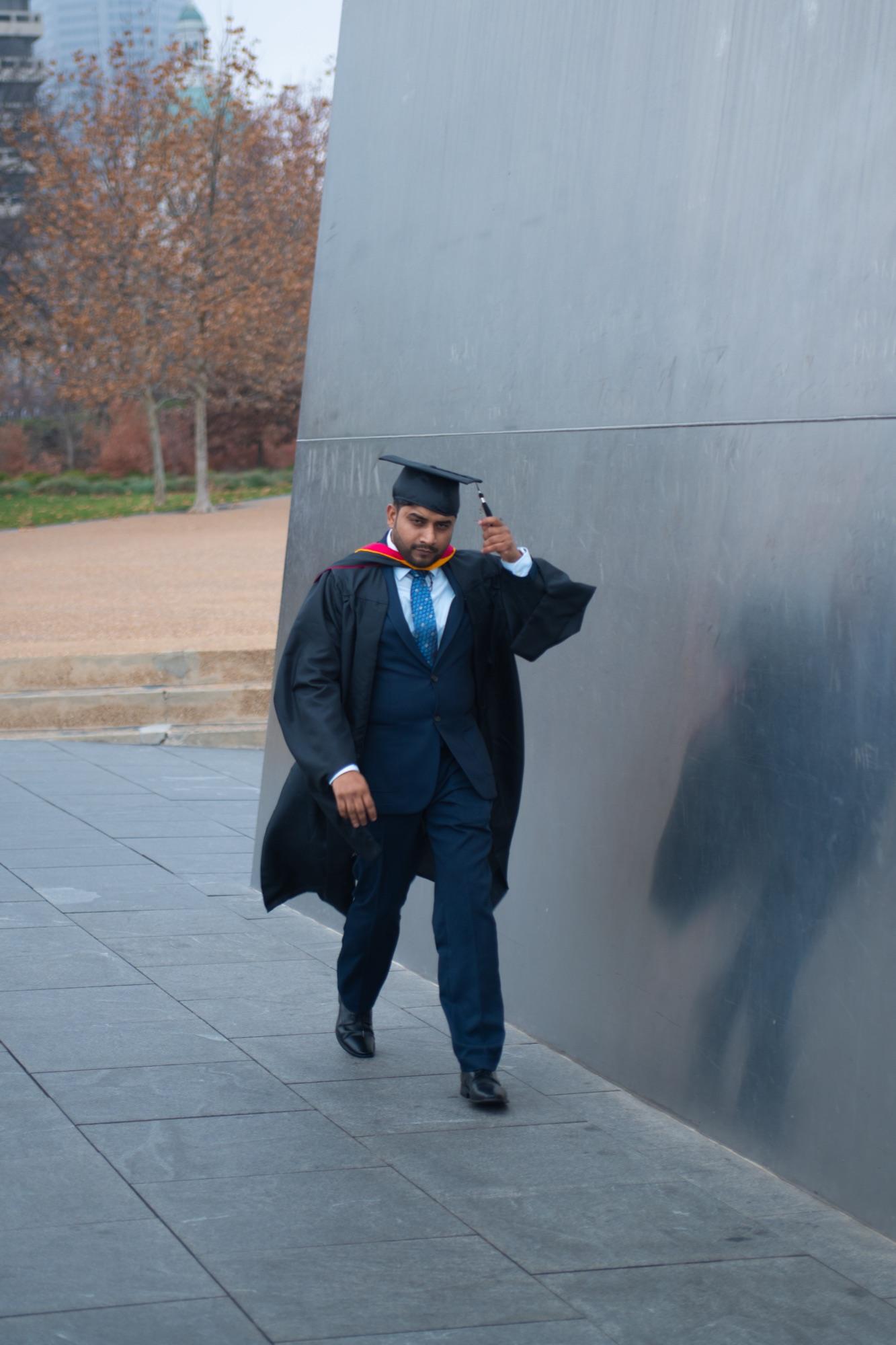 Graduate in cap tipping his hat against the Gateway Arch steel