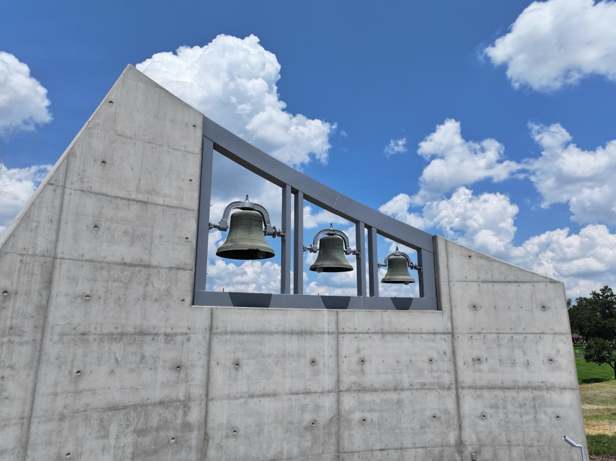 Bronze bells set in the board-formed concrete bell wall of the BSI chapel against a summer sky