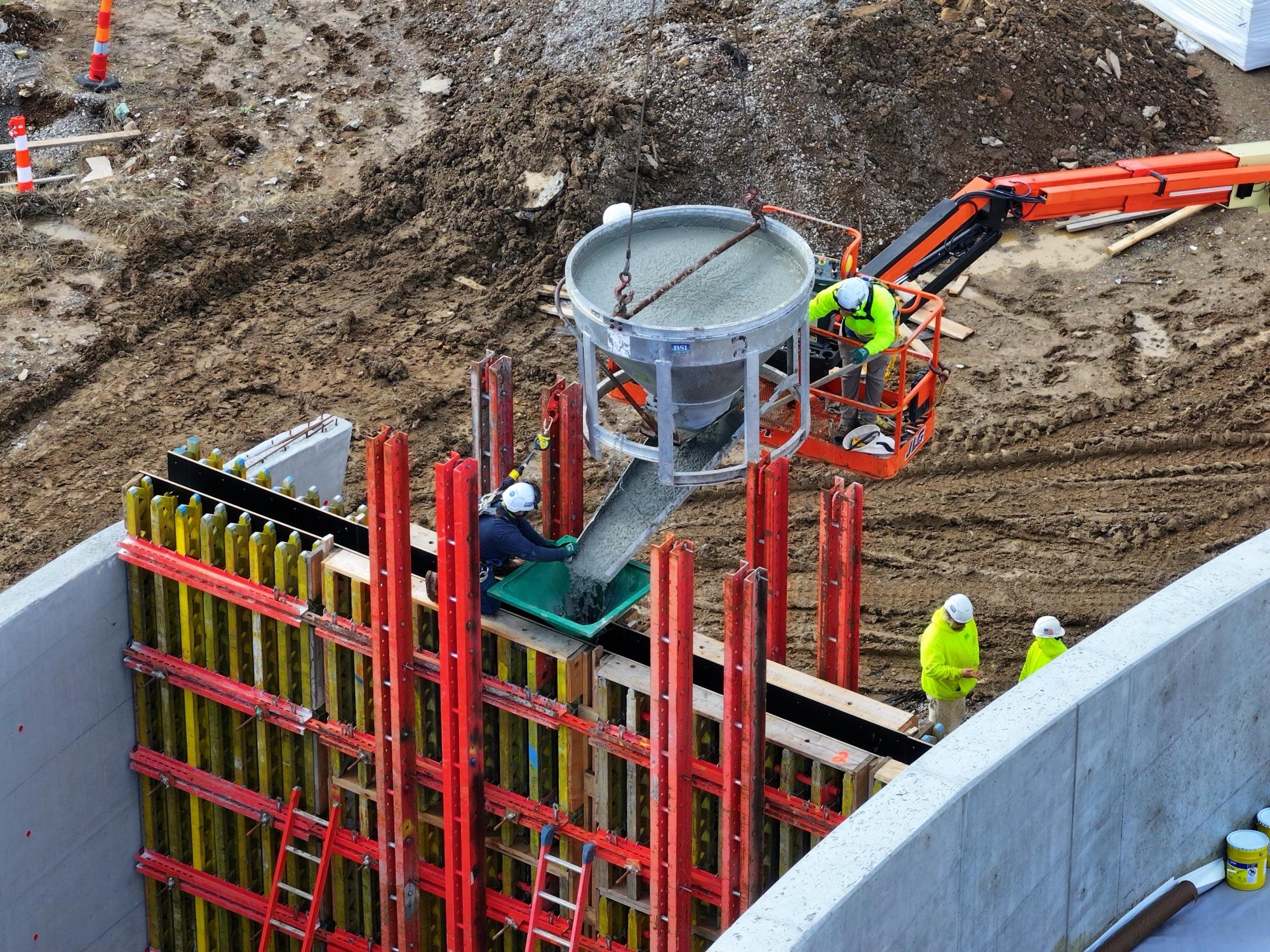 BSI chapel wall pour — concrete bucket over red and yellow formwork, boom lift and crew from above