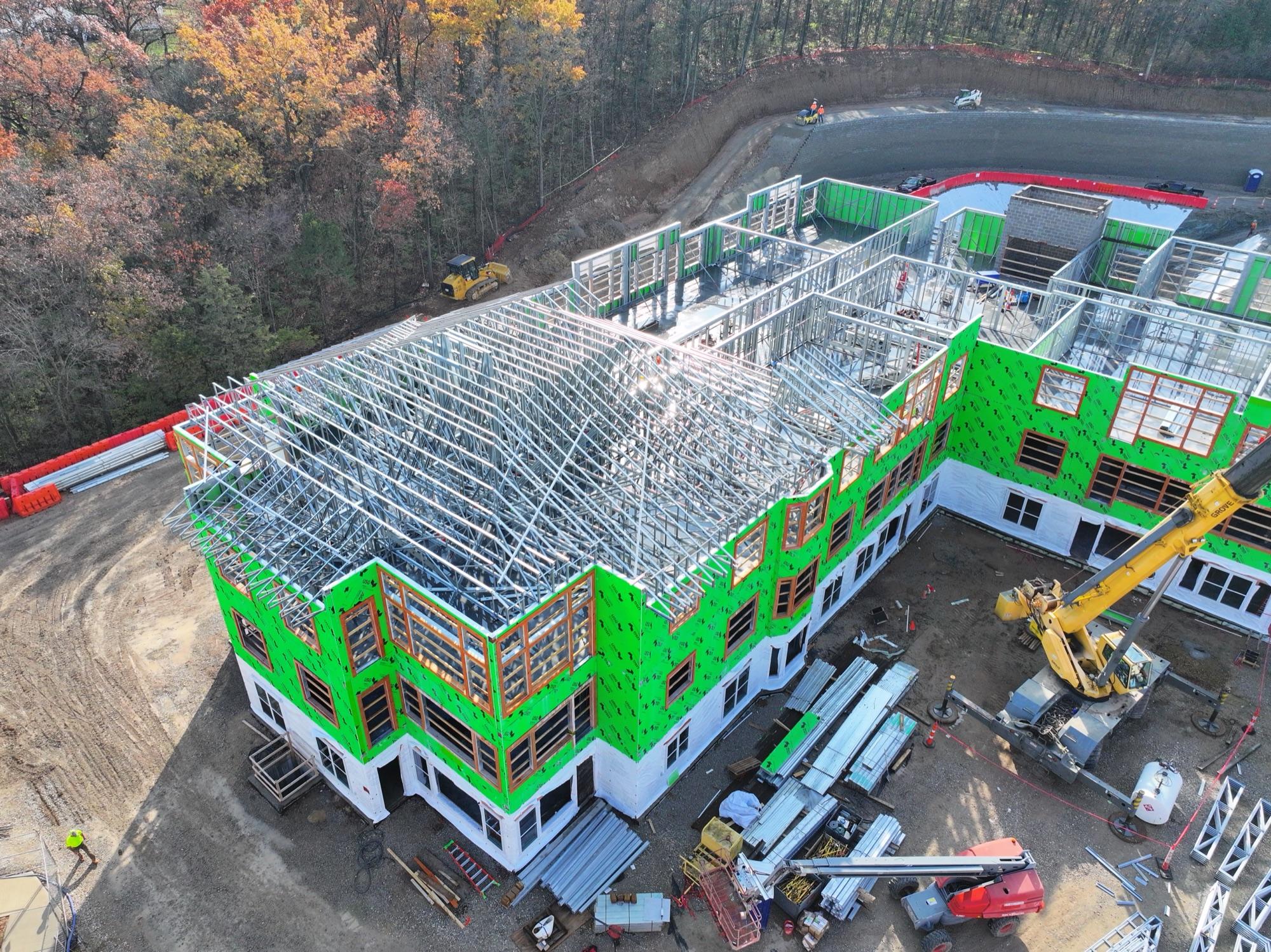 Mason Pointe steel roof trusses over green-sheathed building, crane alongside, autumn treeline behind