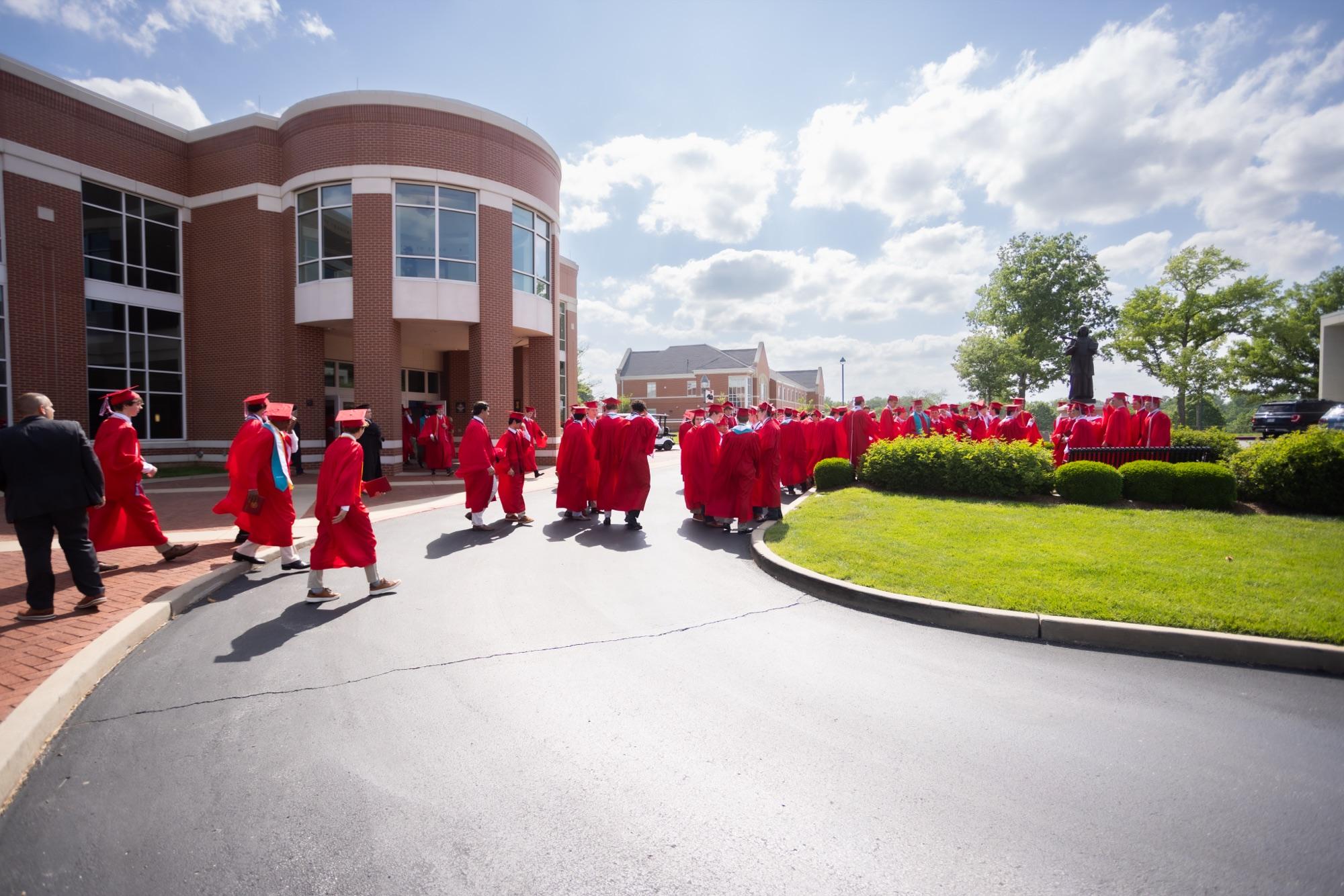 Graduates in red gowns streaming out of a brick campus building after commencement