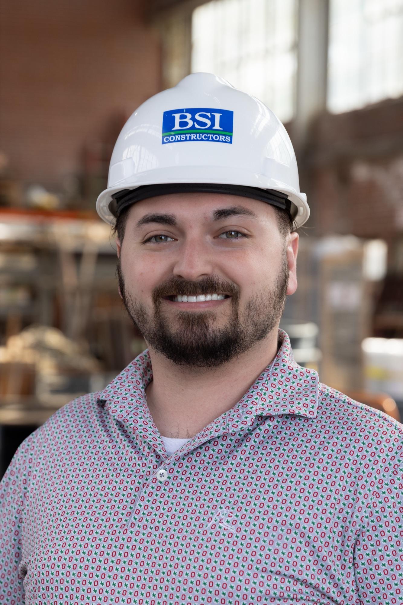 On-site headshot in a hard hat — BSI jobsite bokeh behind